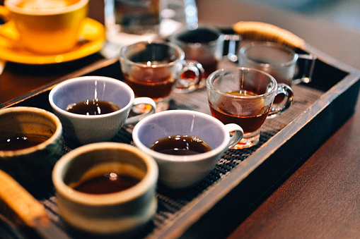 At a coffee testing event, a skillful barista places a wooden tray on the counter, artfully serving four different types of coffee. The tray holds eeight cups, each containing a unique coffee variant - black coffee.