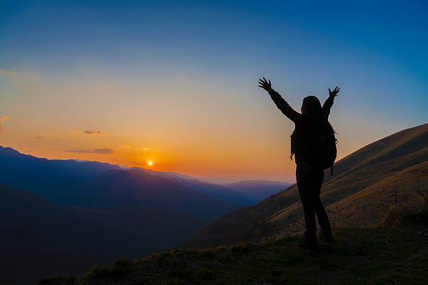 silhouette of female hiker arms raised into sunset stock photo