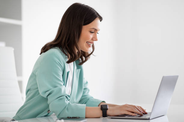 istock Smiling young european lady in suit at table typing on laptop, chatting with client 1788993472