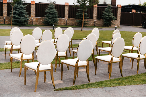 Luxury white-golden chairs on wedding ceremony outdoors. Festive decorations. Empty rows armchairs for guests. Outgoing wedding ceremony in the open air. Decor Studio