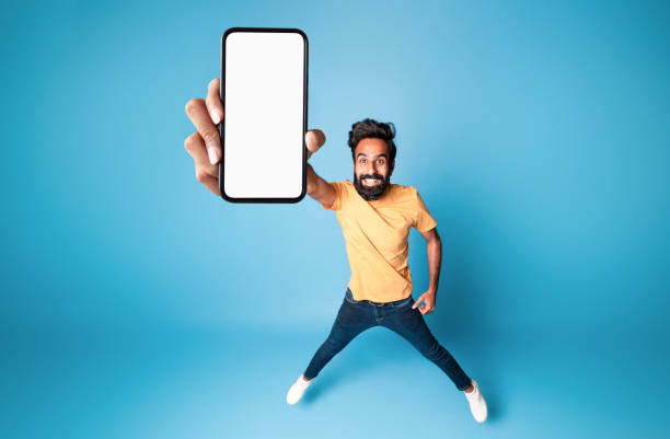 istock Happy indian man showing empty smartphone screen, jumping up over blue background, collage, mockup, above view 1788998028
