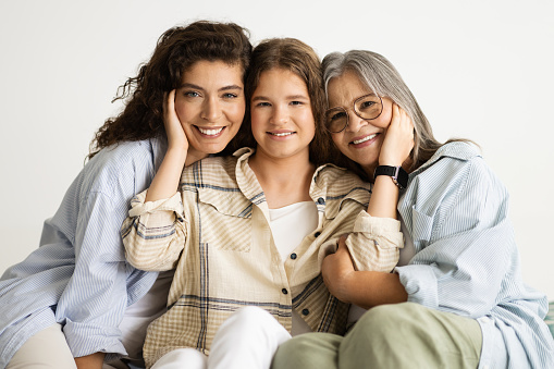 Happy grandmother, mother and daughter sitting on the couch at home