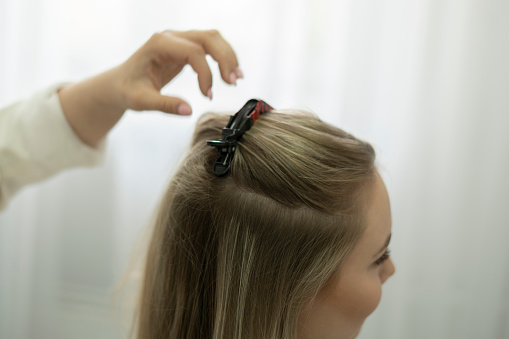 professional hair stylist puts a hairpin in the woman's hair in salon