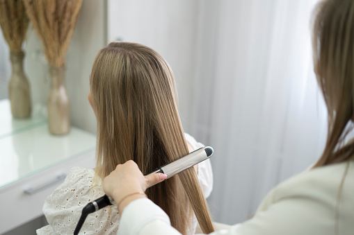 a hairdresser stylist using a Hair straightener to make woman's haircut
