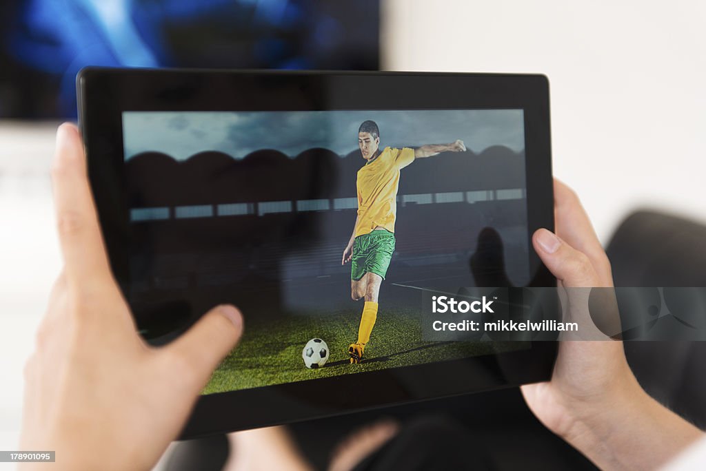 Digital tablet being used to watch a football match Ssoccer game on a digital tablet and football player is about to kick the ball. Concept of streaming live events to a mobile device.  Live Streaming Stock Photo