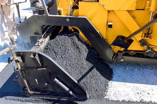 An asphalt paver lays new bitumen asphalt on top of gravel base during construction highway