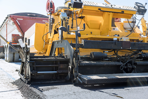 During construction highway concrete paver lays fresh bitumen asphalt on top of gravel base
