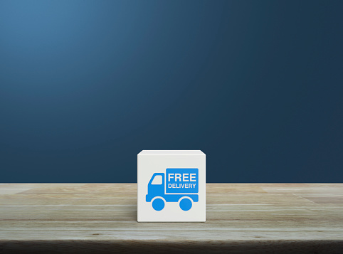 Free delivery truck icon on white block cube on wooden table over light blue wall, Business transportation service concept
