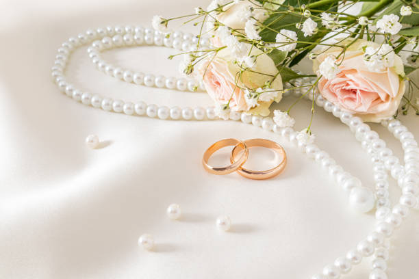 istock Delicate wedding arrangement with two wedding gold rings on a cream satin background with pearl beads and flowers. postcard. invitation. cover. 1789045304