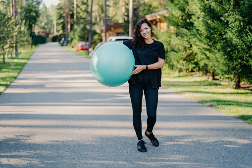 Active woman with fitness ball on a sunny park path, ready for a workout