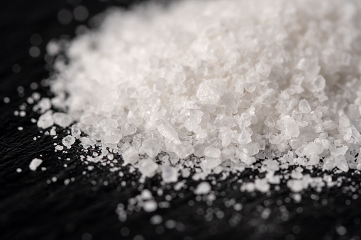 A heap of white salt crystals on a black stone background. Food