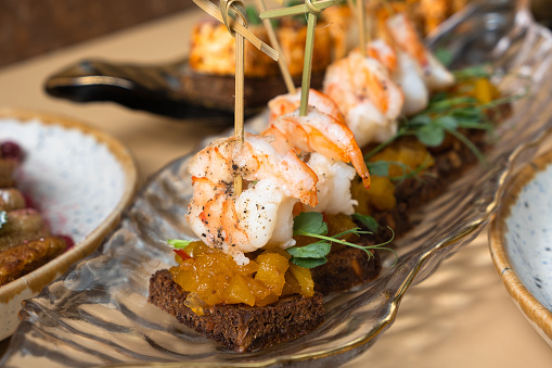 Close up shrimp and mango chutney canapes in glass plate. Mini sandwiches and other dishes.