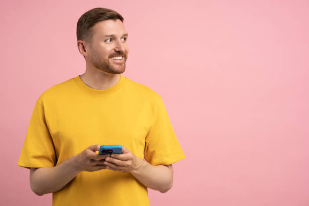 istock Happy cheerful guy holding smartphone interested looking away standing aside empty blank studio wall 1789112095