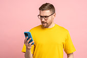Wondered bearded man in glasses looking at mobile phone screen in surprise shocked at message, news