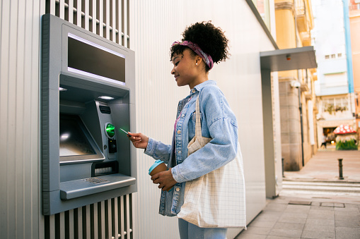 Beautiful young multiracial woman taking the money from the ATM machine for shopping.