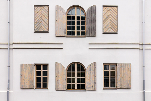 White building wall with many arched windows and wooden shutters on it