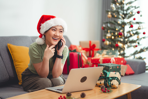 Asian woman enjoy with working online and talking on phone at home on Christmas day. Happy woman working from home.