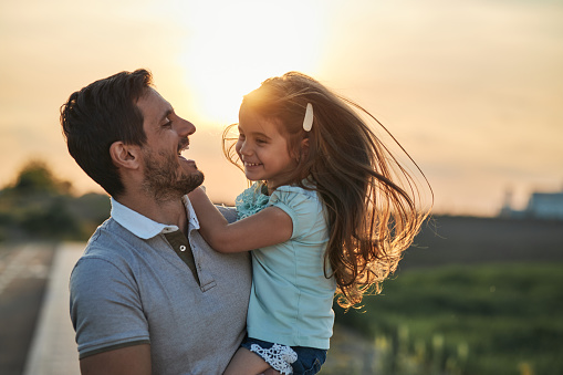 Young father and daughter in field on a sunset. Single father is carrying little girl.