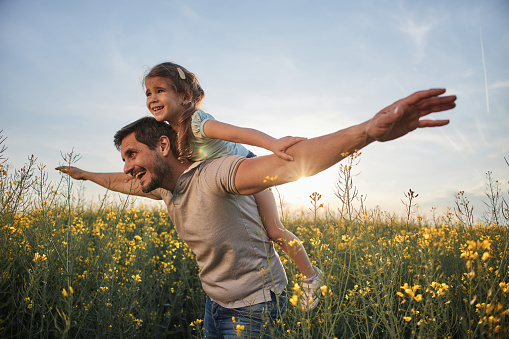 Young father and daughter in field on a sunset. Single father is carrying little girl.