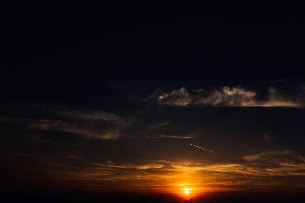 die orangefarbene sonne verschwindet hinter den wolken und der spur aus dem flugzeug - vapor trail sky night sunset stock-fotos und bilder