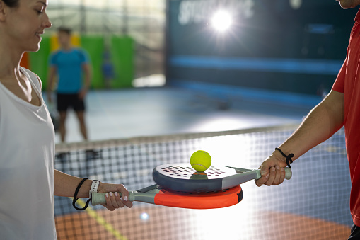 Close-up shot of young couple holding rackets and ball before playing paddle tennis match on indoor court
