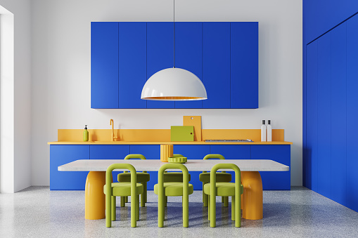 Colorful hotel kitchen interior with stone eating table and green chairs, light concrete floor. Cooking room with blue cabinet, kitchenware and big lamp. 3D rendering
