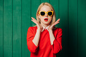 Suprirsed stylish woman in sunglasses and red dress on green wooden background