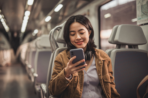 Young beautiful Chinese woman traveling by subway, using mobile phone to surf the internet or pay online ticket, she is in the train car