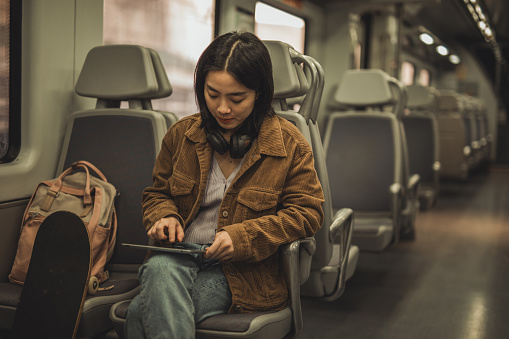 A young beautiful Chinese woman is traveling in the subway, she is using a digital tablet to surf the internet or shop online to make her travel time pass faster, she is in the carriage