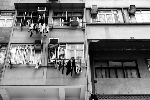In the heart of urban contrast, a black and white photograph captures a moment frozen in time—a modest, weathered building stands stoically with laundry dancing on lines, a testament to the resilience of daily life.