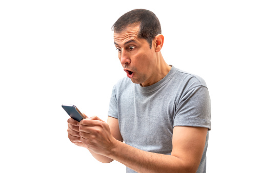 Latin man receiving surprising news on line in a smart phone with white background