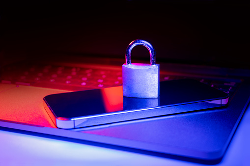 Closeup of a padlock on a laptop and phone illuminated with blue and red light.Phishing, cybersecurity danger or ransomware attack. Encrypted privacy in email.