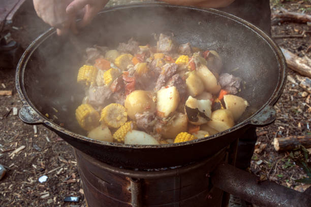 Large pieces of meat, ears of corn, potatoes and vegetables are fried in a cast-iron cauldron on an outdoor wood-burning stove. Street food