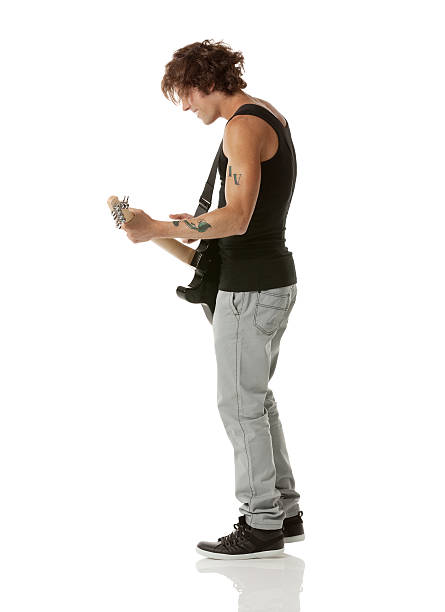 Tatooed man standing behind with electric guitar, studio shoot in white backgground