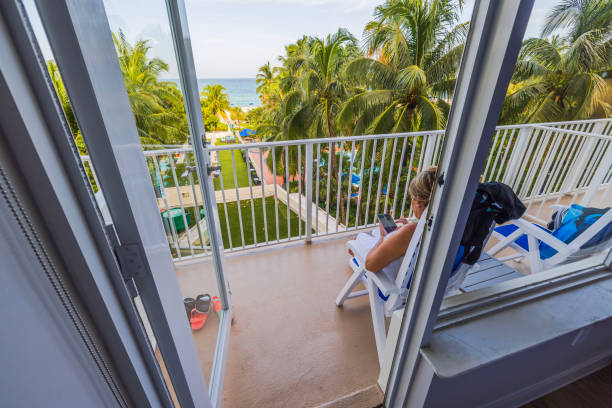 Beautiful view of hotel room interior with open balcony overlooking Atlantic Ocean, where woman sits in chair and surfs on her phone. Miami Beach. USA. Beautiful view of hotel room interior with open balcony overlooking Atlantic Ocean, where woman sits in chair and surfs on her phone. Miami Beach. USA. 1 hotel south beach stock pictures, royalty-free photos & images