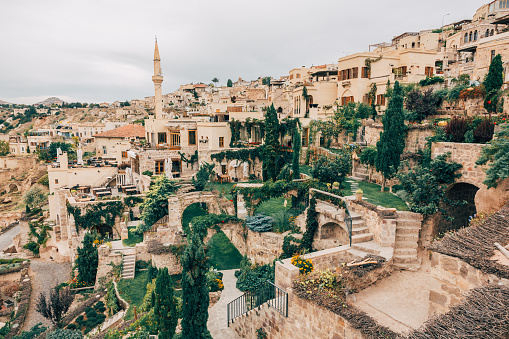 A breathtaking view of Cappadocia, capturing unique stone houses, lush green terraces, and an imposing minaret. The historic essence of the town is beautifully framed against the scenic rolling hills.