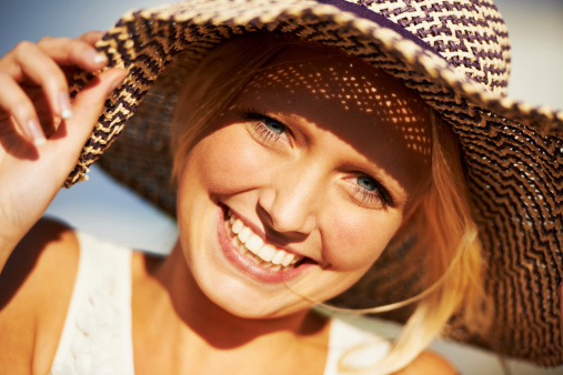 Happy woman in dress and straw hat making photo on retro camera while sitting on grass outdoors