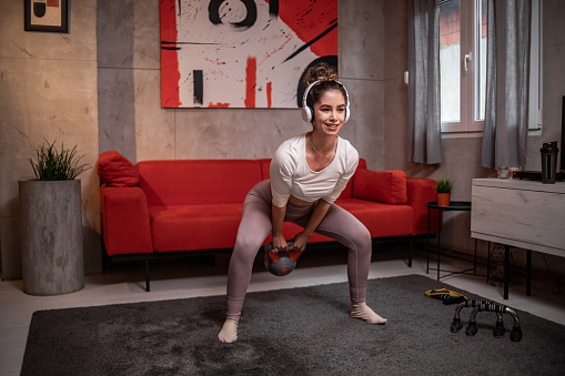 A beautiful young woman, an athlete, is doing sports exercises in her apartment, she is doing squats