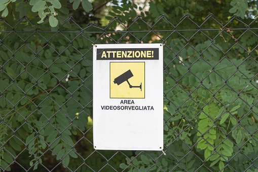 CCTV security camera sign on a chain link fence in a park.