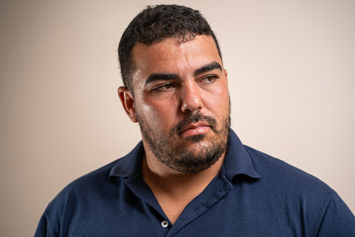 Man with dark hair and beard looking to the side with serious expression on pastel background.