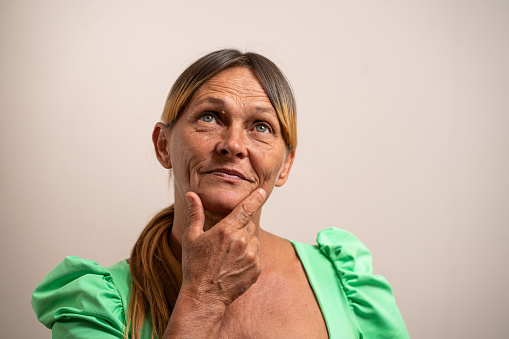 Middle aged woman thinking with hand on chin on pastel background.