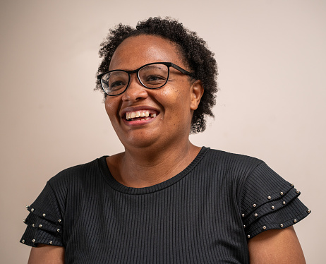 Black woman wearing glasses smiling on pastel background.