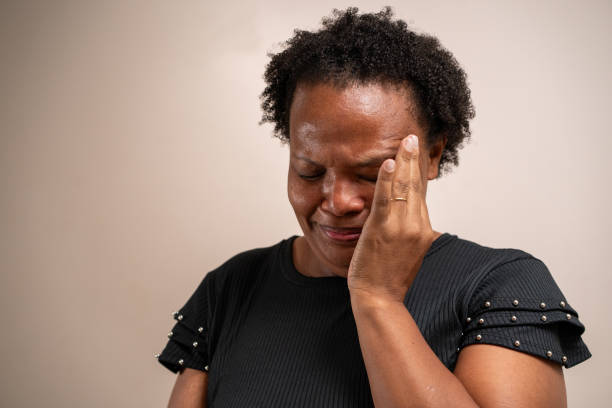 Black woman with hand on face crying on pastel background.