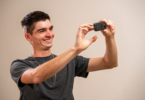 Young man taking photo with a 360 camera on pastel background.