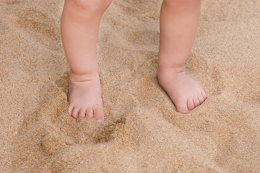 Tiny baby feet on the sand beach close up with copy space