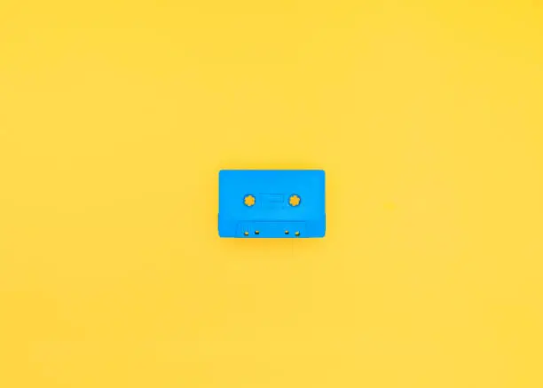 Retro and vintage blue cassette tape centered on a bright yellow background. Studio shot with copy space.