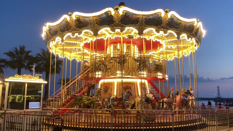 Golden illuminated retro carousel turning in amusement park. Shiny merry-go-round glowing and rotating at night. Festival atmosphere of funfair.