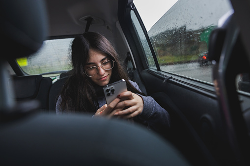 Teenage girl using the smartphone inside the vehicle during a rainy day.