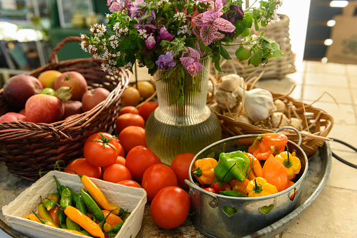 Very rustic sales stall with tomatoes, apples, peppers, and flowers. Big tray at a farm shop with fresh, organic fruit and vegetables