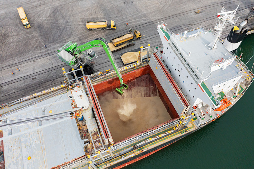 Top view of a large cargo ship loading or unloading grain. Sea transportation. Truck carrying grain